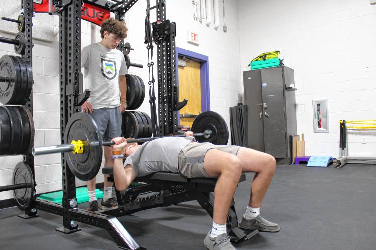 Pioneer Valley Regional School junior Jayden Tyler warms up on the bench, while Joey Seaman looks on in the school’s newly renovated auxiliary gym.