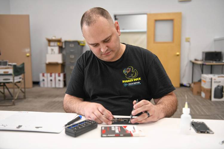 Rubber Duck Tech Repair owner Daniel Adams replaces a battery in a cellphone at the Greenfield business, which has moved to Suite 23 at Mohawk Mall, 91 Main St.