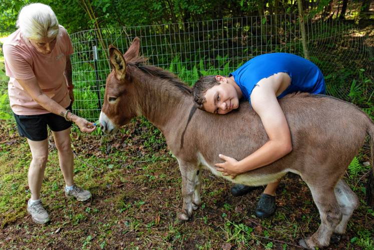 Tricia Hamilton, co-owner of Jefferson’s Safe Haven in Leverett, offers a treat to Nester, a donkey at the sanctuary, while Keenan Hamilton gives the donkey a hug. The sanctuary now takes care of 35 animals on a 3-acre site in Leverett. 