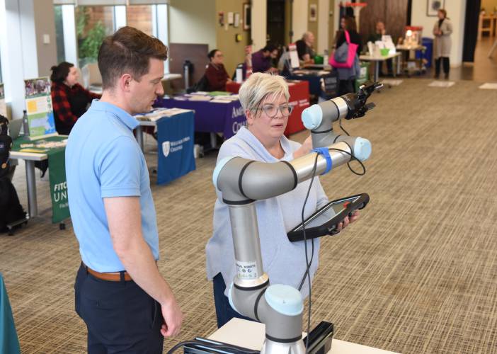 Nathan Desrochers of Universal Robotics lets Kristin Cole, vice president of workforce development for Greenfield Community College, program a robotic arm at GCC in 2022. Thanks to a $200,000 grant, GCC will develop training programs in mechatronics, or robotic engineering, and industrial machine maintenance that Cole says will “get folks ready for those new jobs that are going to continue to come down the pike, related to automation and robotics.”