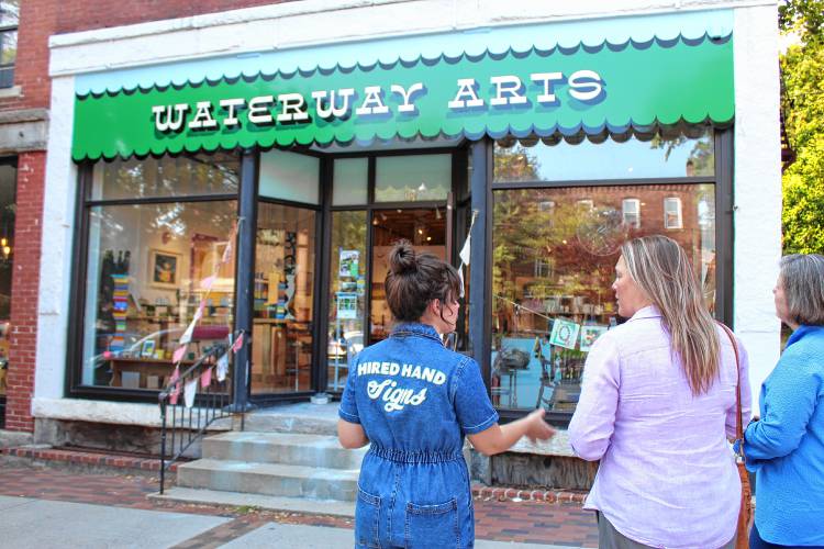 Signmaker Jess Marsh Wissemann, left, shows state Sen. Jo Comerford, right, and state Rep. Natalie Blais, center, signs she has made around Turners Falls on Friday. The Waterway Arts sign is one of her favorite creations so far.