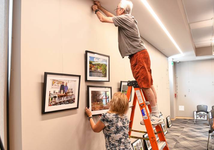 Barbara Krawczyk and Kevin Fay of the Springfield Photographic Society hang photos depicting Franklin County municipalities in the meeting room of the Greenfield Public Library. The photos are on display through Nov. 30.