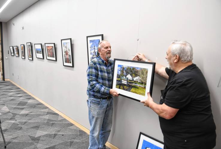 East Longmeadow resident Richard Harper and Ludlow resident Jack Grimaldi, both members of the Springfield Photographic Society, hang photos depicting Franklin County municipalities in the meeting room of the Greenfield Public Library. The photos are on display through Nov. 30.