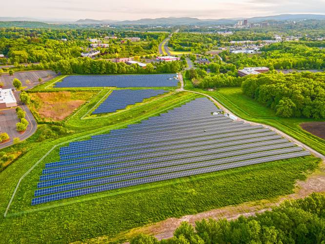 An aerial view of Nexamp’s Hadley 3 solar site between the Hampshire Mall to the left and the U.S. Fish and Wildlife regional headquarters to the right, looking north toward the University of Massachusetts Amherst in the distance.