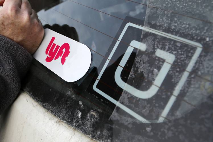 A Lyft logo is installed on a Lyft driver’s car next to an Uber sticker in Pittsburgh in 2018. Ballot Question 3 asks Massachusetts voters if they approve of a proposed law that would allow drivers for Lyft and Uber, and any other companies that use a digital network to connect riders to drivers for pre-arranged transportation, to collectively bargain to create negotiated recommendations concerning wages, benefits, and terms and conditions of work. 