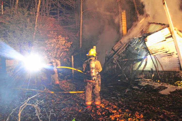 Firefighters from six departments work to knock down a Shelburne Falls shed fire that spread to the woods behind 18 South St., up to the railroad tracks, on Tuesday evening.