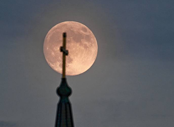 The cross atop the steeple of the Holy Trinity Church on Main Street in Greenfield is silhouetted against the backdrop of the nearly full moon Thursday evening. 