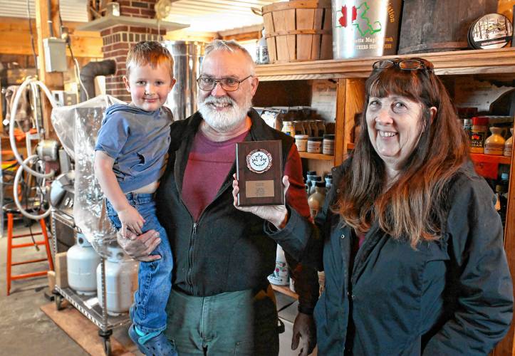 Howard Boyden holds grandson John Boyden, 3, while his wife Jeanne Boyden holds their most recent award at their sugarhouse in Conway this week. The Boydens were awarded second place for their golden/delicate syrup during the annual North American Maple Syrup Council competition.