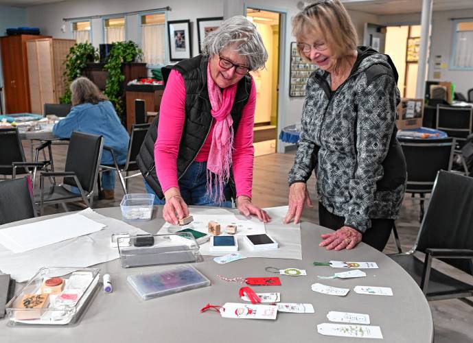 Northfield resident Joanne Gardner is assisted by Barbara King, right, who was leading a workshop on crafting tags for holiday gifts held at the Northfield Senior Center on Tuesday.