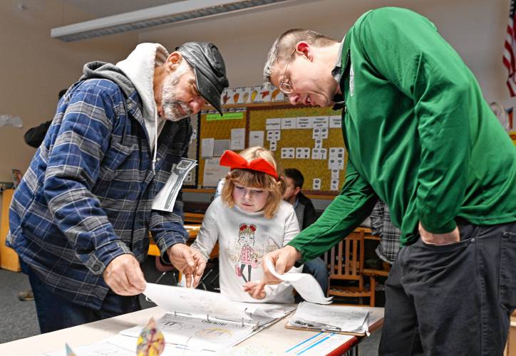 Serria Higgins, center, a first grade student in Libby Keller’s class at Warwick Community School, shows her grandfather Michael Brown, left, and Principal Stephen Stroud, fossil drawings during the school’s Community Exhibition of Learning on Friday afternoon.