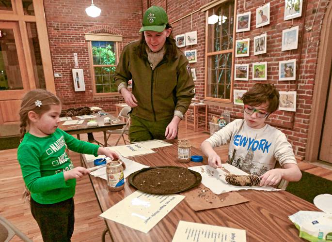 Sara Griffin, 6, and her brother Phineas, 9, of Northfield, make bird feeders by coating pine cones with sun butter and seeds under the instruction of Wren Wood, center, a park interpreter at the Great Falls Discovery Center, as part of “It’s a Wonderful Night in Turners Falls” on Friday.